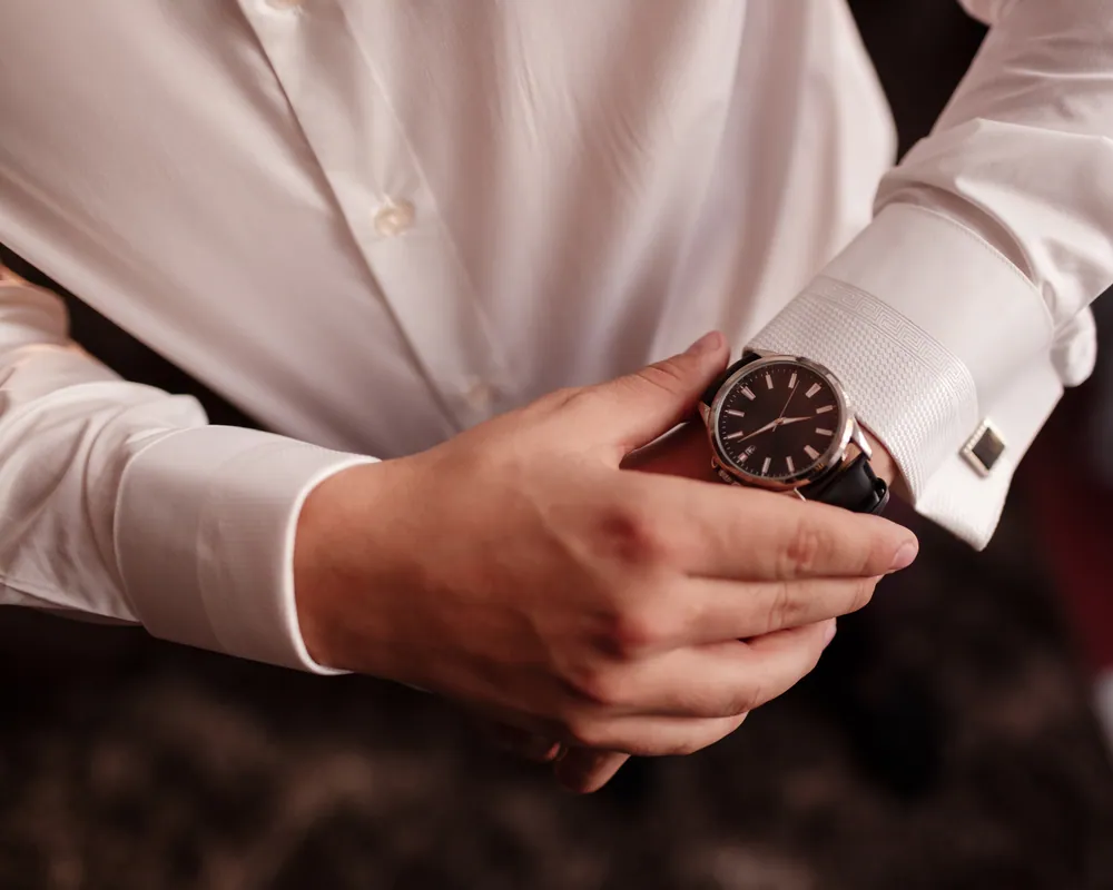 Detalle de un reloj de pulsera y gemelos sobre una camisa blanca