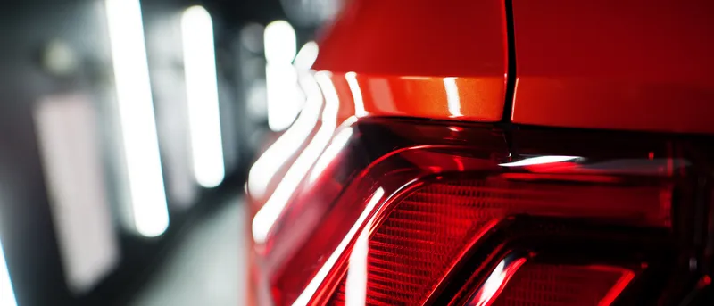 Primer plano del piloto trasero de un coche rojo de lujo, con la carrocería reflejando la luz.