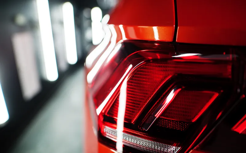 Primer plano del piloto trasero de un coche rojo de lujo, con la carrocería reflejando la luz.