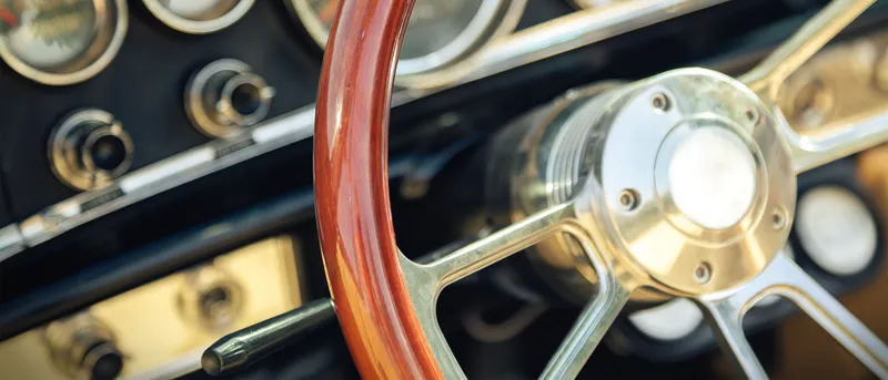 Interior de un coche clásico con volante de madera y salpicadero de cuero.