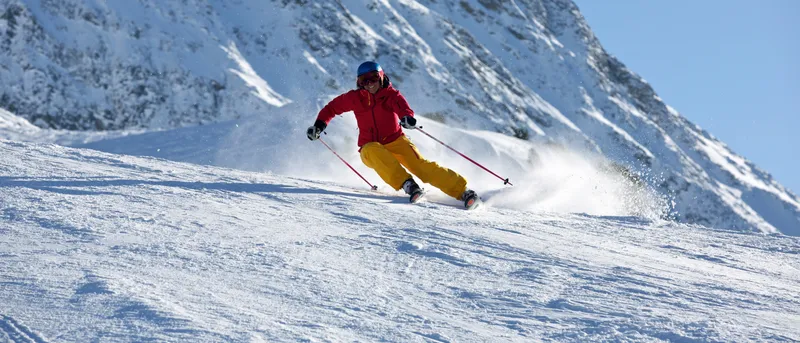 Esquiadora descendiendo una pista nevada en el Tirol austriaco bajo un cielo despejado.